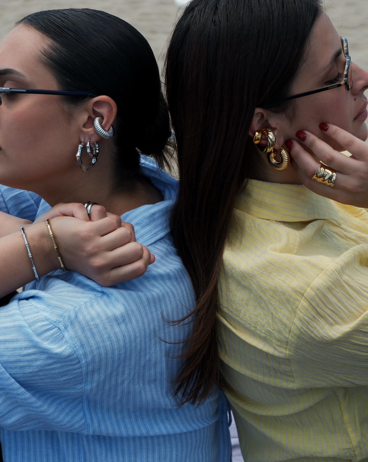 Due modelle indossano bijoux Dudu con orecchini, anelli e bracciali in oro e argento dal design contemporaneo.